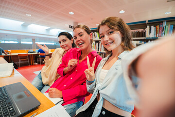 Three cheerful young women happily taking a selfie together while enjoying their time as students in a library, showcasing their friendship and joy in this moment of camaraderie and fun
