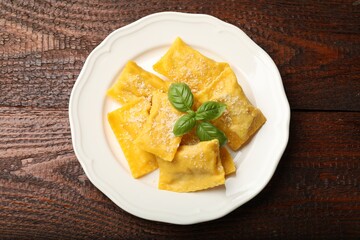 Delicious ravioli with parmesan cheese and basil on wooden table, top view
