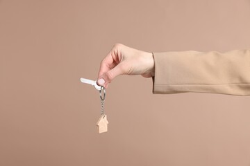 Real estate agent holding key with house shaped keychain on beige background, closeup