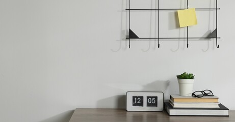 Stationery, flip clock, floral decor and glasses on wooden office table near white wall