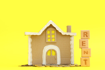Toy house with coins and word RENT on yellow background