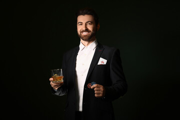 Handsome young man with whiskey and poker chips on dark green background
