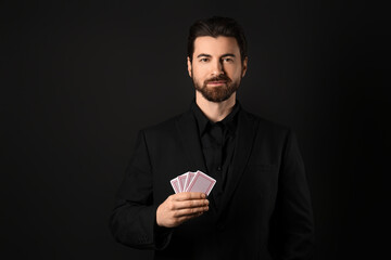 Handsome young man with playing cards for poker on black background