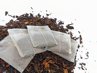 Close-Up of Five Dry Tea Bags Lying on a Pile of Loose Leaf Black Tea, Displaying Natural Texture...