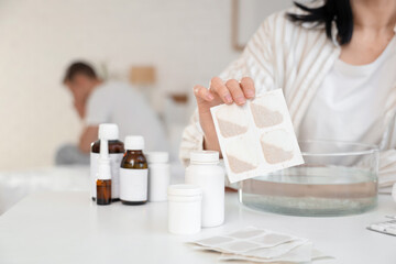 Young woman dipping mustard plaster into bowl of water for her ill husband in bedroom, closeup