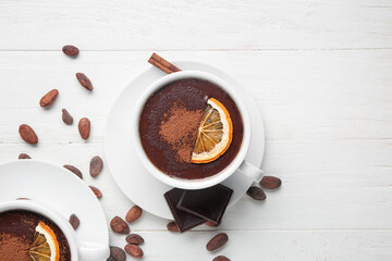 Cups of hot chocolate with cocoa beans and dried orange slices on white wooden background