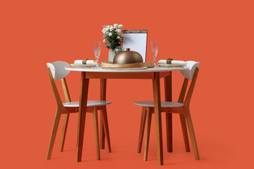 Restaurant table for two with cloche, flowers and menu on orange background