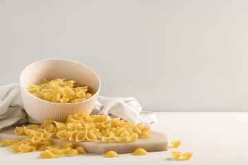 Bowl and tray with raw pasta shells on white background