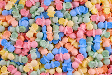 Colorful pacifier-shaped candy in pastel hues creates a playful, sweet background. Ideal for baby shower themes, childhood nostalgia, candy promotions, or confectionery product design.