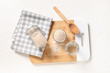 Board with psyllium husk powder and glass of water on white background