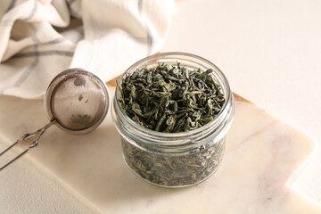 Jar with dried green tea leaves and strainer on white background
