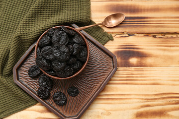 Bowl and tray with dried prunes on wooden background