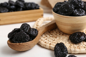 Bowl and spoon with dried prunes on white wooden background