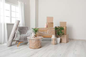 Wrapped furniture with stretch film, plants and boxes in room on moving day