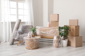 Wrapped furniture with stretch film, plants and boxes in room on moving day