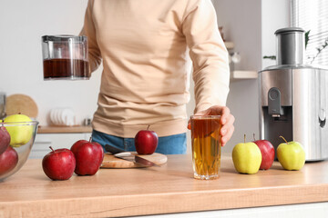 Young man with fresh juice and apples at table in kitchen, closeup