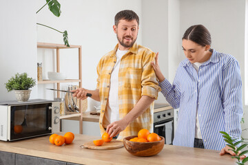 Young man cutting orange and his quarreling wife in kitchen