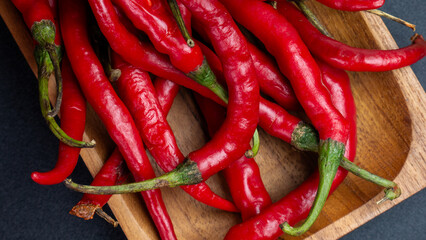 Flat lay of a pile of fresh red chilies with natural green stems on a wooden tray. Suitable for cooking or culinary articles