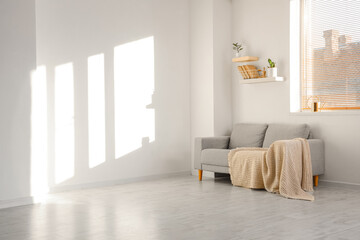 Interior of light living room with grey sofa, shelves and window