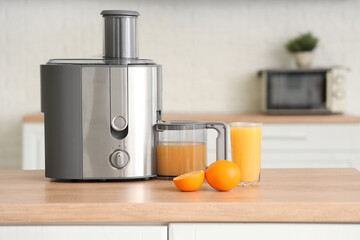 Modern juicer with fresh oranges on table in kitchen