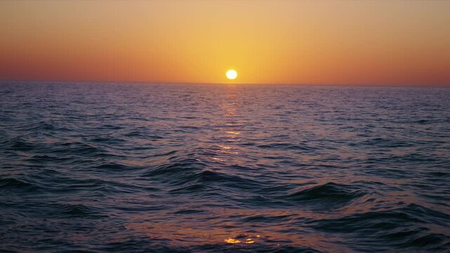 Witness the breathtaking beauty of a serene sunset as the sun peacefully sets over calm ocean waves, showcasing an array of vibrant colors and promoting a sense of tranquility in slow motion