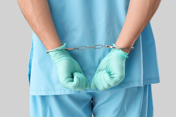 Handcuffed male doctor on light background, back view