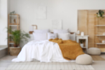 Blurred view of light bedroom with folding screen, shelf units and plants