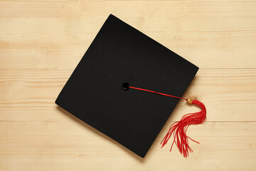 Graduation hat on wooden background, top view