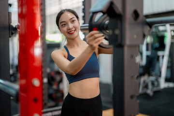 Fototapeta premium Asian sportswoman adding weights on barbell in gym