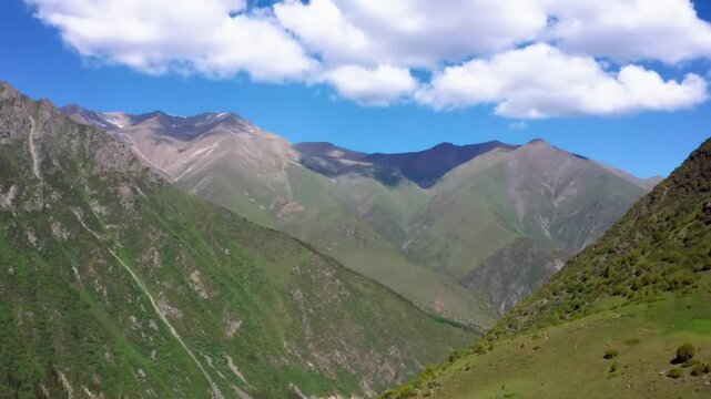 This footage captures the breathtaking view of green mountains with clouds hovering over the peaks, showcasing the natural beauty of Ala Archa National Park, Kyrgyzstan.