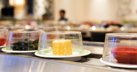 Plates with corn, seaweed, and other colorful ingredients are rotating on a conveyor belt in a kaiten zushi restaurant, offering a modern and efficient dining experience