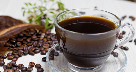 Steaming cup of black coffee sits on a wooden table, surrounded by roasted coffee beans spilling from a burlap sack, creating a warm and inviting scene for coffee lovers