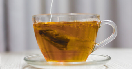 Brewing tea in a glass cup, with the tea bag string gently hanging down, creates a warm and comforting beverage resting on a white wooden table, inviting moments of relaxation