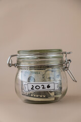 Glass jar full of American currency dollars cash banknote with text 2026 year. Preparation saving money. Moderate consumption and economy. Collecting money
