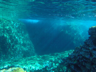 Dark blue ocean surface seen from underwater. Abstract waves underwater and rays of sunlight shining through, Sun light rays undersea deep, Underwater background with sea bottom, Mediterranean sea.