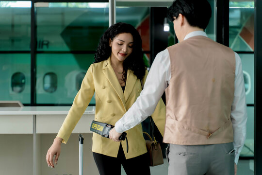 Airport security officer performing manual scan with handheld metal detector on female passenger during pre-boarding safety check at departure gate
