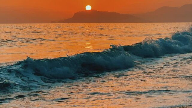 Sunset in Turkey, Alanya. The waves of the Mediterranean Sea roll over the sandy beach. The sunset is reflected in the water and slightly illuminates the city, against the background of Castle Hill.4К
