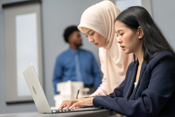 Obraz premium Professional business discussion between two female colleagues using laptop in modern office, teamwork collaboration, diverse workplace, technology in business, professional attire, strategic planning