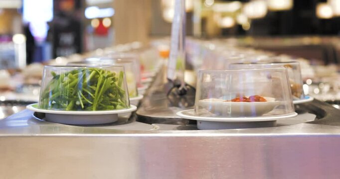 Seafood, chinese cabbage, and green vegetables gliding on kaiten sushi conveyor belt, offering fresh ingredients for diners preparing hot pot meal