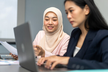 Professional business discussion between two female colleagues using laptop in modern office,...