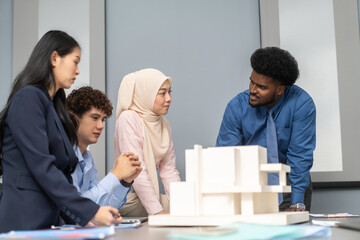 Architects engineers collaborating on building design project in modern office, diverse team of professionals female muslim architect and male engineers discussing architectural model of structure