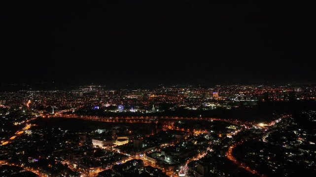 Drone shot of the city glowing like a galaxy under the night sky, buzzing with life and light
