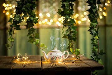 Steaming Tea Pot On Wood Table With Ivy And Fairy Lights Backdrop