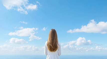 Obraz premium A woman with long hair is standing in front of a blue sky with clouds
