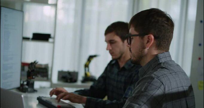 Two young software developers working together on a project, analyzing code on a monitor in a modern workspace. Concept of teamwork, coding, and software development.