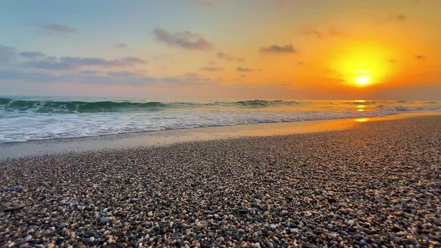 Sunset in Turkey, Alanya. The waves of the Mediterranean Sea roll over the sandy beach. The sunset is reflected in the water and slightly illuminates the city, against the background of Castle Hill.4К