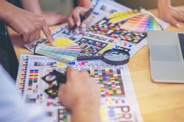 Team graphic designer checking print quality of media graphics proof print and color guides in...