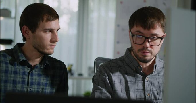 Two young developers working together on a programming project in a well-lit workspace. Collaboration, concentration, and teamwork in tech.