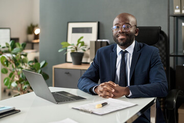 Obraz premium Portrait of African American manager smiling at camera while sitting at his workplace in office
