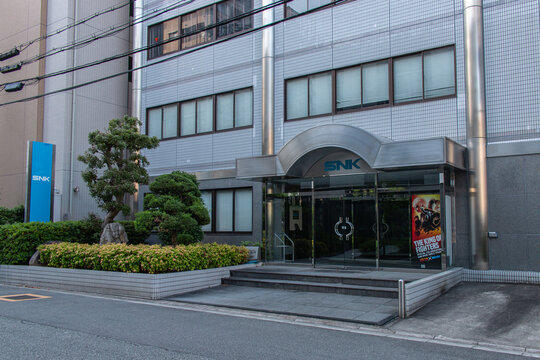 Suita, Osaka, JAPAN - May 22 2022 : Street view of SNK's company office in Suita, featuring a modern building entrance and King of Fighters promotional poster.